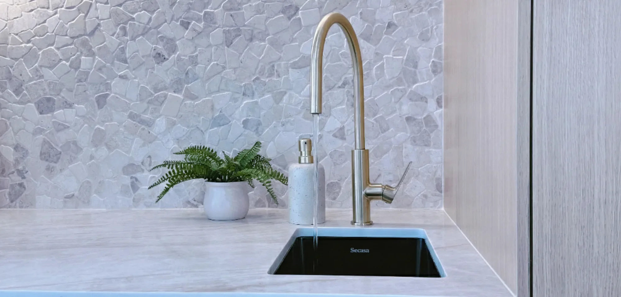 Modern kitchen sink with brushed gold mixer tap and stone benchtop, featuring Secasa black inset sink and decorative tile splashback