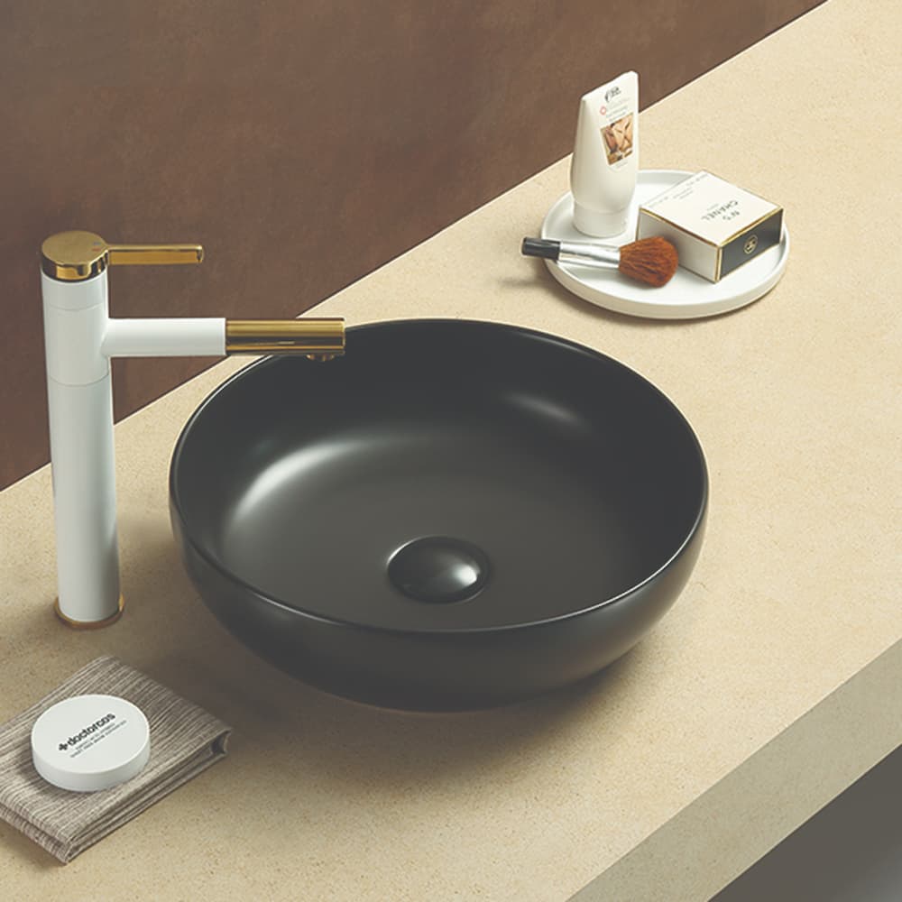 Oban Fine Ceramic Above Counter Basin in Matt Black finish with white and gold faucet on a beige surface