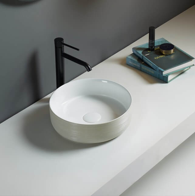 Lukka Ollia fine ceramic above counter basin in round shape, gloss white finish with clay line art pattern, 346×346×114 mm, non-overflow, 32 mm waste on a gray countertop with a black faucet.