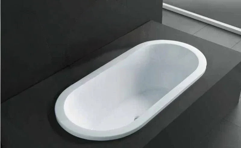 Simple modern built-in white bath installed in a minimalist grey tiled bathroom