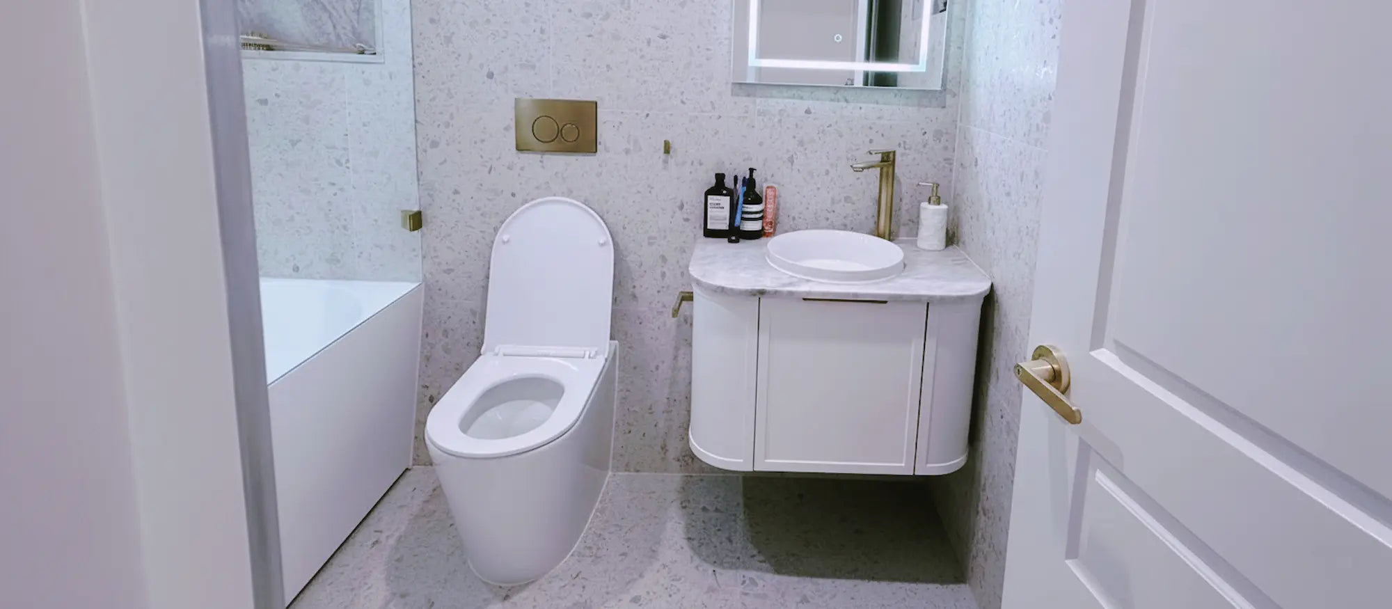 Modern bathroom with wall-hung vanity, round countertop basin, back-to-wall toilet, LED mirror and brushed gold tapware.