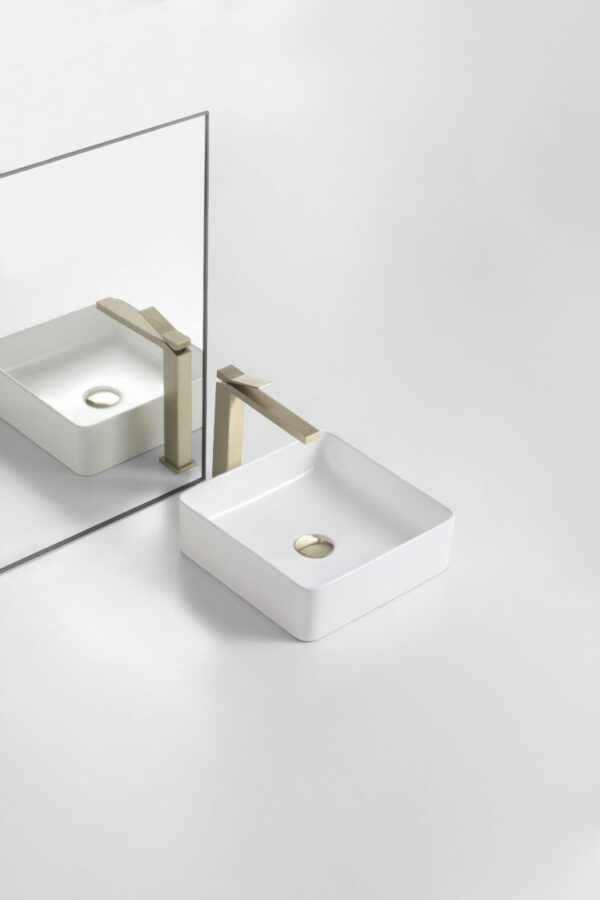Modern square white bathroom vanity basin with brushed gold tapware on a white surface, reflected in a mirror. Secasa Home style.