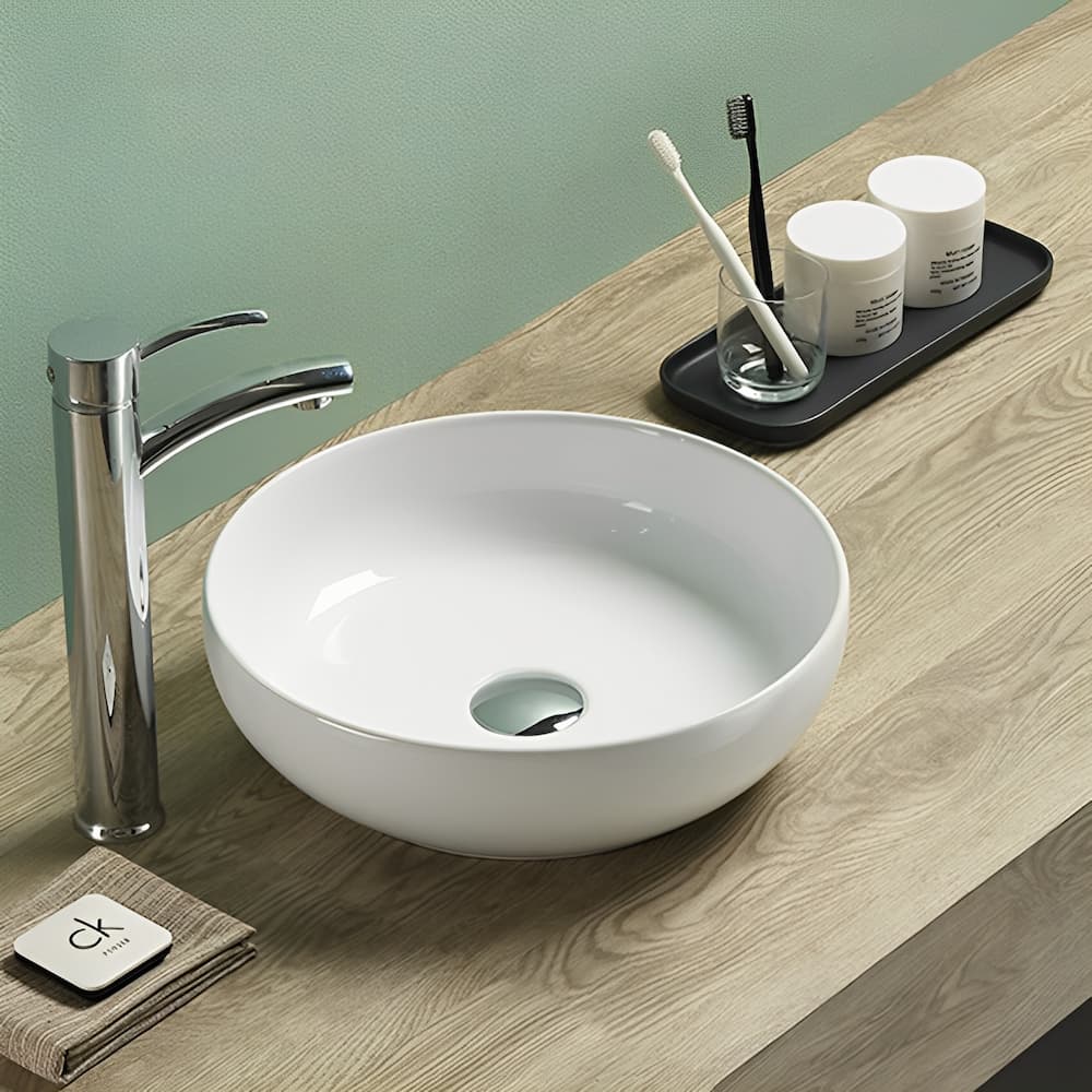 Oban Fine Ceramic Above Counter Basin in Gloss White finish, chrome faucet, and toiletries on a wooden countertop.