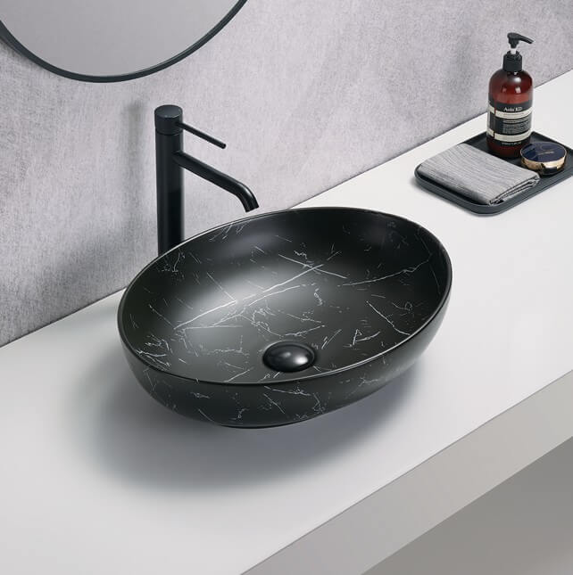 Lukka CAREY fine ceramic above counter basin in matt marble black finish, 520x395x130mm, modern countertop basin design on a bathroom counter with a faucet and toiletries.