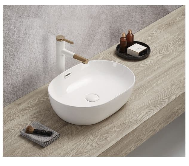 Lukka Ellips oval fine ceramic above counter basin (LK-ELA490 series) in Gloss White on a wooden countertop with a faucet and toiletries.