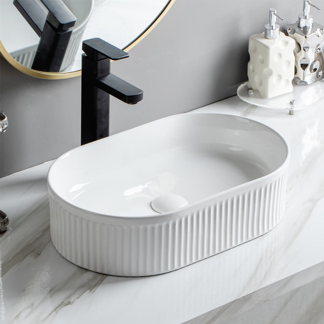 Lukka Ellips Fluted Fine Ceramic Above Counter Basin in oval shape gloss white with black faucet in a bathroom setting