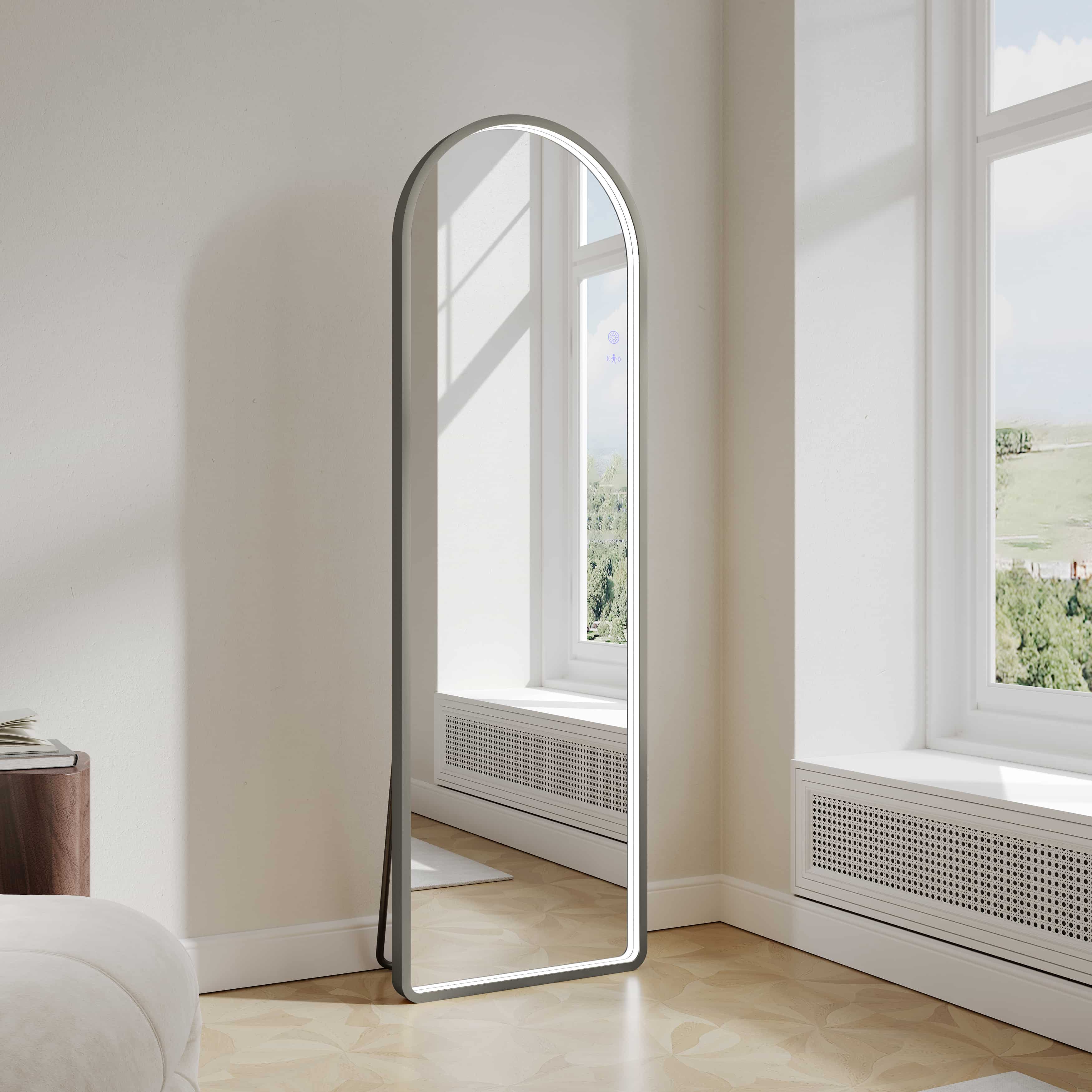 Modern arch LED freestanding mirror in gun metal finish by window in bright room